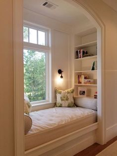 a window seat in the corner of a room with bookshelves and pillows on it