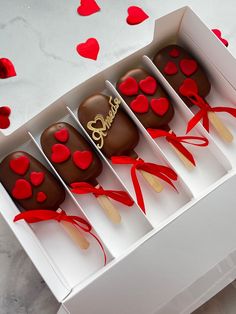 four chocolate covered candys in a box with red ribbon and hearts on the side