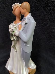 a figurine of a bride and groom kissing on the cheek with black background