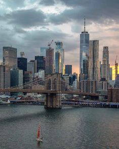 a sailboat on the water in front of a large city with tall buildings under a cloudy sky