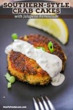 a black plate topped with crab cakes covered in white sauce and garnished with green onions