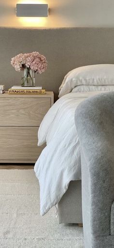 a white bed sitting next to a nightstand with flowers on top of it in a bedroom