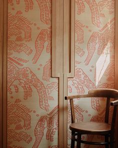 a wooden chair sitting in front of a wall with red and white designs on it