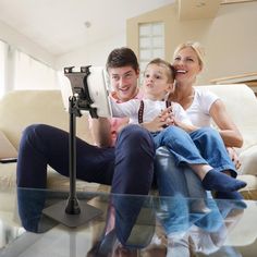 a man, woman and child are sitting on a couch looking at a tablet computer