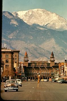 an old town with mountains in the background and cars parked on the street near it