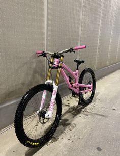 a pink bike leaning against a wall in front of a gray wall with white and yellow lettering