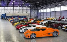 an orange sports car is parked in a large garage with other cars and trucks behind it