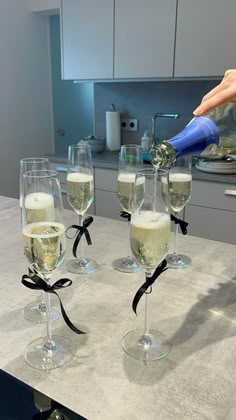 a person pouring champagne into wine glasses on a kitchen counter with black ribbon around them