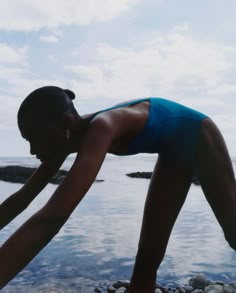 a woman bending over on rocks by the water