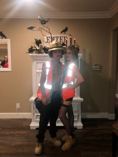 two people wearing safety vests and hats standing next to each other in front of a fireplace