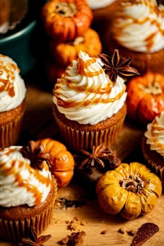 several cupcakes with icing and pumpkins around them on a wooden table