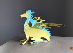 a yellow and blue paper dragon sitting on top of a gray table next to a black wall