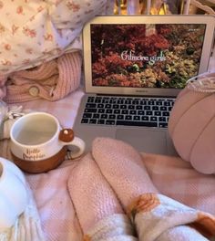 an open laptop computer sitting on top of a bed next to pillows and blankets,