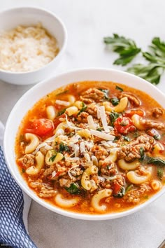 a white bowl filled with pasta and meat soup on top of a blue towel next to a spoon