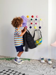 a little boy standing in front of a wall mounted coat rack with balls on it