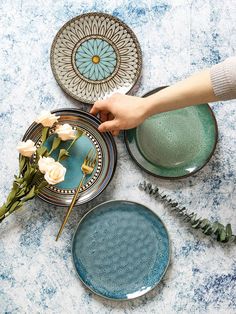 a table topped with plates and flowers on top of a blue marble countertop next to plants