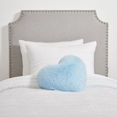 a blue heart shaped pillow sitting on top of a bed next to white sheets and pillows