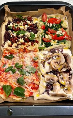 four different types of pizzas in a box with basil, tomatoes, mushrooms and other toppings