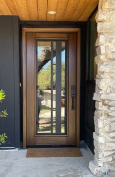 a wooden door with glass on the front of a house next to a stone wall