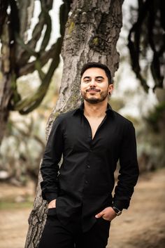 a man standing next to a tree with his hands in his pockets and looking at the camera