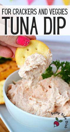 a hand holding a cracker over a bowl of tuna dip