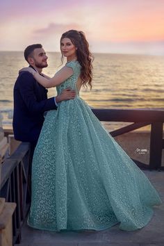 a man and woman standing next to each other in front of the ocean at sunset