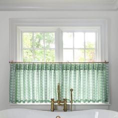 a bath tub sitting next to a window with green curtains on the windowsills