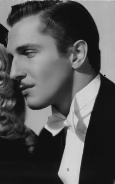 a black and white photo of a man in a tuxedo next to a woman with curly hair