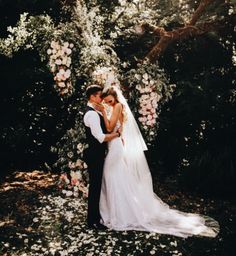 a bride and groom standing in front of an arch of flowers