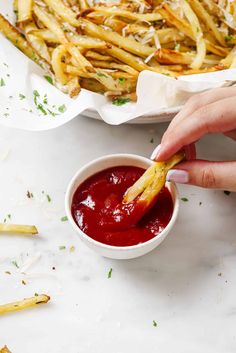 a person dipping something into a small white bowl filled with ketchup and french fries