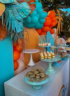 dessert table with orange, blue and white balloons on the wall behind it at an outdoor party