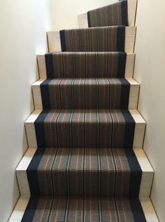 a carpeted stair case with blue and red stripes on the bottom, next to a white wall