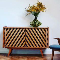 a vase with flowers sitting on top of a wooden cabinet next to a blue chair