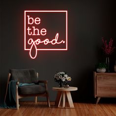 a neon sign that says be the good in front of a black wall with a chair