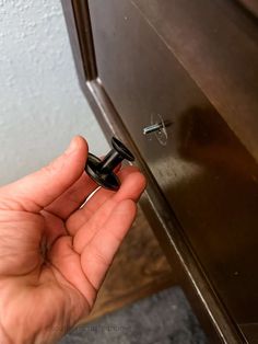 a hand is holding an open door with a screw in it and there are two keys on the handle