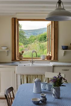 a kitchen with a sink, window and table in front of an open window that looks out onto the countryside