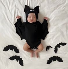 a baby wearing a bat costume laying on a white sheet with black bats around it