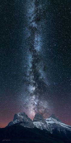 the night sky is filled with stars above mountains and snow - capped peaks in the distance