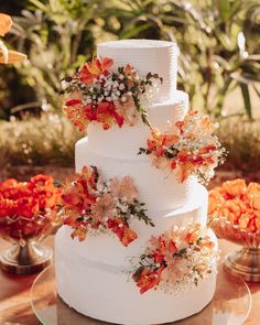 a white wedding cake with orange flowers on the top and bottom tier is sitting on a table