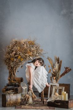 a woman in white dress standing next to an arrangement of dried plants