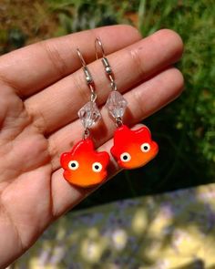 a hand holding two orange fish shaped earrings