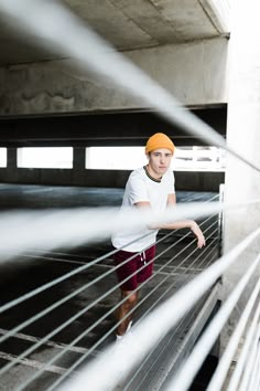 a young man standing on top of a bridge next to a metal railing and wearing a yellow hat