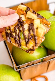 a person is holding up a piece of fruit with chocolate and nuts on it in front of some green apples