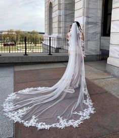 a woman in a wedding dress is standing on the sidewalk with her veil blowing in the wind