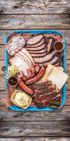 a blue tray topped with lots of meats and other foods on top of a wooden table