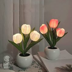 two white vases with flowers in them sitting on a table next to a book