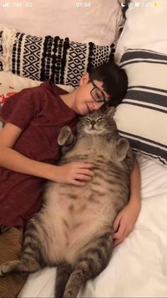 a young boy laying on top of a bed next to a large gray and white cat