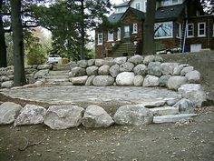 there is a rock wall and steps in front of the house with trees around it