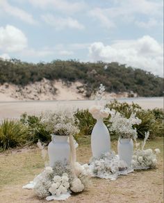 three white vases with flowers on the ground