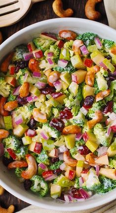 a white bowl filled with broccoli, apples and cranberries next to nuts